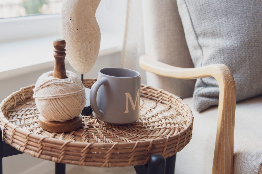A gray mug with the letter M sits on a woven round table next to a ball of twine and a wooden holder. The scene is beside a cushioned chair and a window, giving a cozy, sunlit atmosphere. Housing developer marketing photography internal and external lifestyle photography Manchester, Leeds and Liverpool